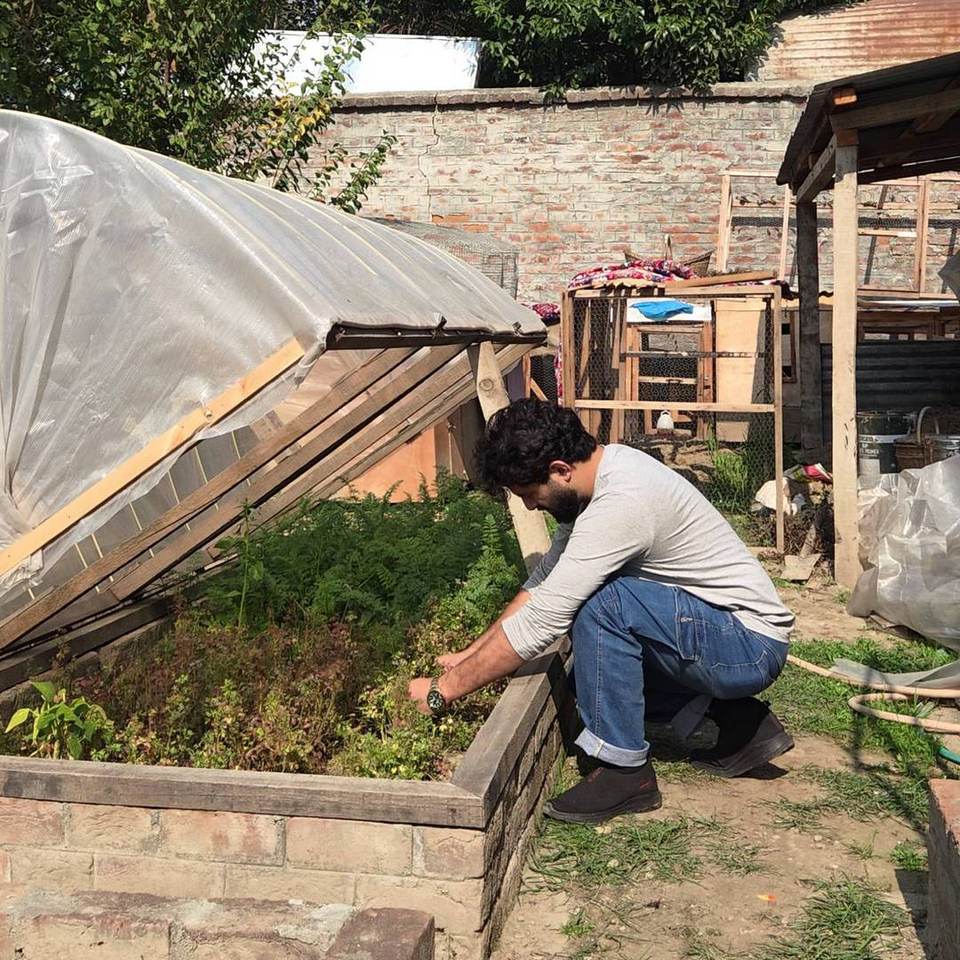 Rabet crouching beside the open tunnel, tending the vegetables in the raised bed